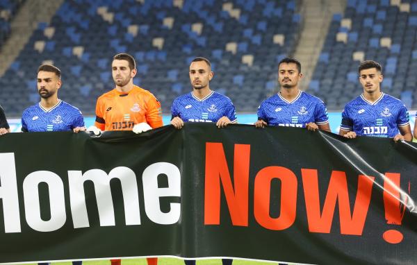 שחקני הפועל פתח תקוה עם שלט Bring Them Home Now למען שחרור החטופים. מימין - רועי אלימלך, מתן פלג, מתן גושה, עומר כץ, רם לוי