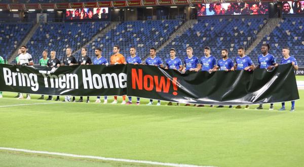 שחקני הפועל פתח תקוה עם שלט Bring Them Home Now למען שחרור החטופים