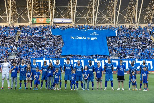 שחקני הפועל פ"ת לקראת פתיחת משחק העלייה, על רקע אוהדי הפועל פ"ת ביציע המזרחי של איצטדיון ראש הזהב
